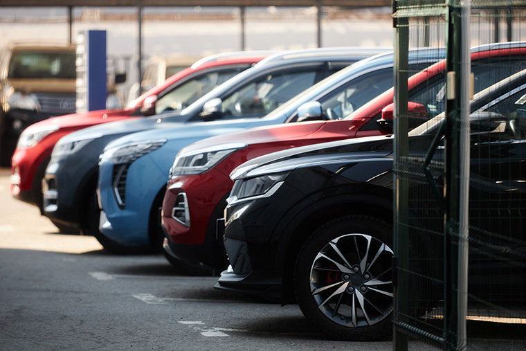 Row of modern SUVs in various colours, including black, red, and blue, parked diagonally in an outdoor lot with a metal fence partially visible in the foreground.