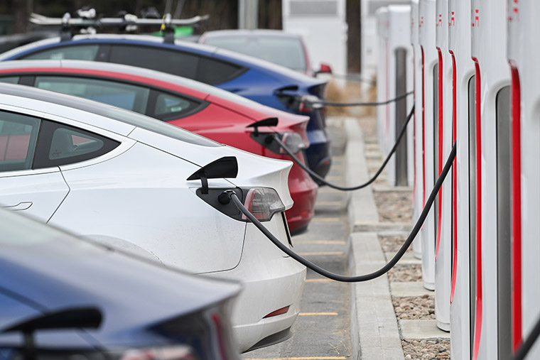 Electric vehicles charging at a station, lined up in a parking lot with charging cables connected.