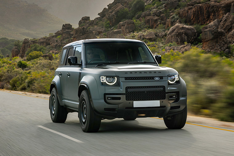 Front side view of a Range Rover Sport driving on an open road with a mountainous backdrop. The SUV showcases its sleek design.